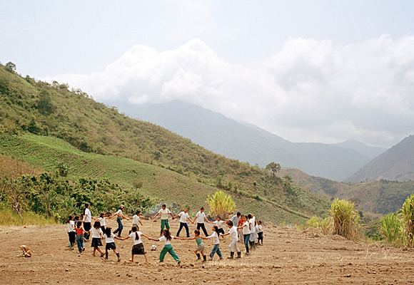 photograph of children playing in a circle on land that's been cleared